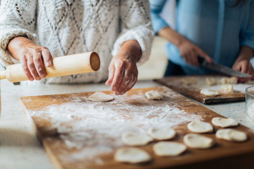 Homemade dumplings being prepared on a floured board with hands and rolling pin.